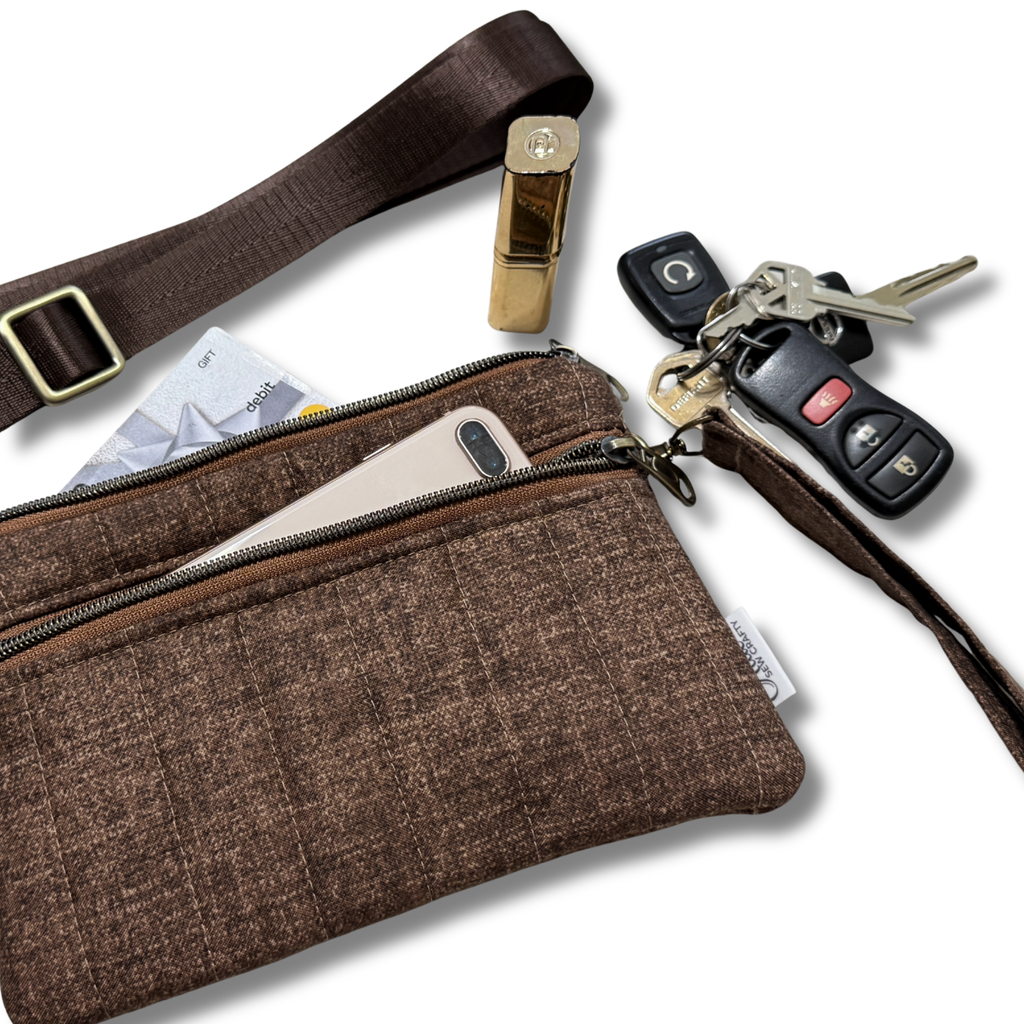 A brown textured fabric crossbody bag with a matching wrist strap, shown with a phone, card, lipstick, keys, and car key fob in its pockets on a white background.
