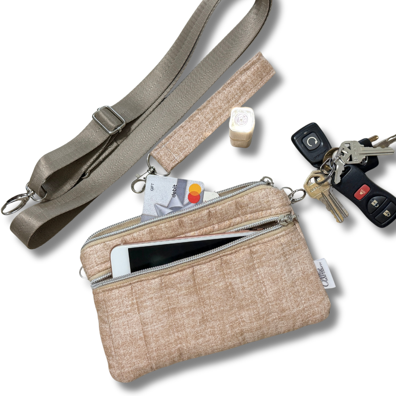 A beige woven crossbody bag with a zippered front pocket and an adjustable shoulder strap, shown on a white background with accessories including keys, a card, and a phone partially inserted.