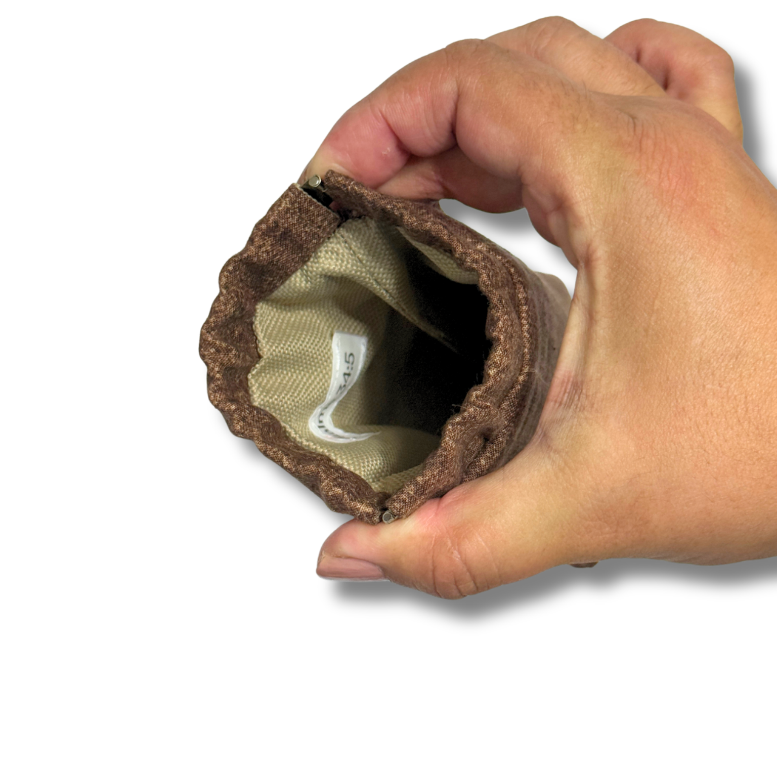 A close-up of a hand holding an open brown fabric pouch with a tan interior lining, shown against a plain white background.