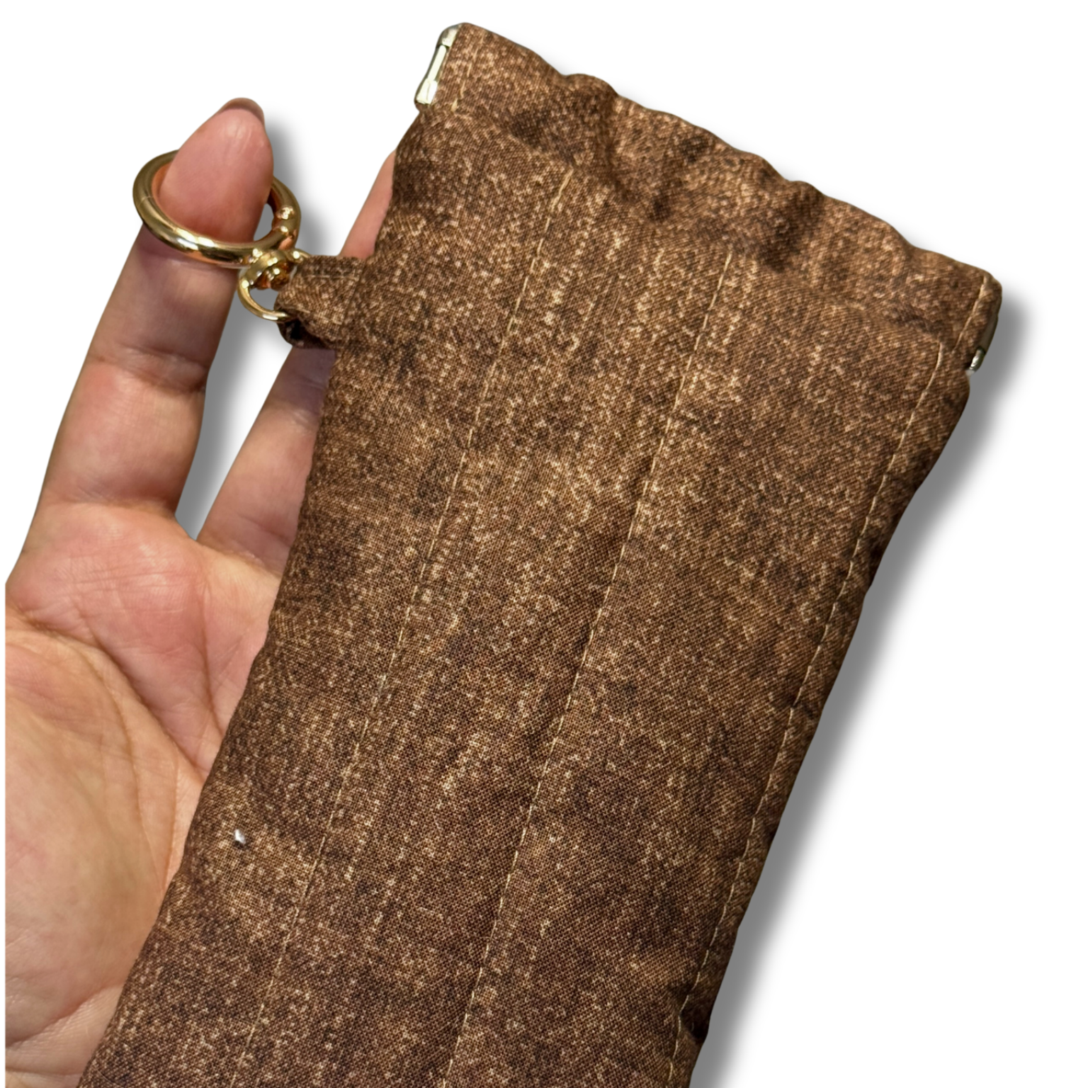 A close-up of a hand holding a brown textured sleeve or pouch with a gold-tone key ring attachment, shown against a plain white background.