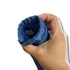 A close-up of a hand holding the opening of a blue textured fabric snap-on bag, showing the interior lining and a tag 