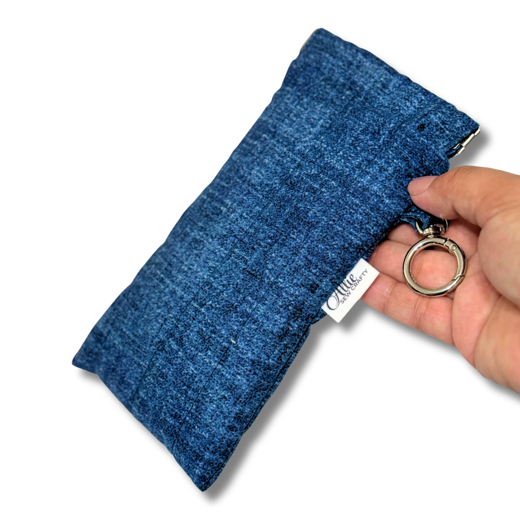 A hand holding a blue denim pouch with a silver metal key ring and a white fabric tag that reads 'Allie Sew Crafty'