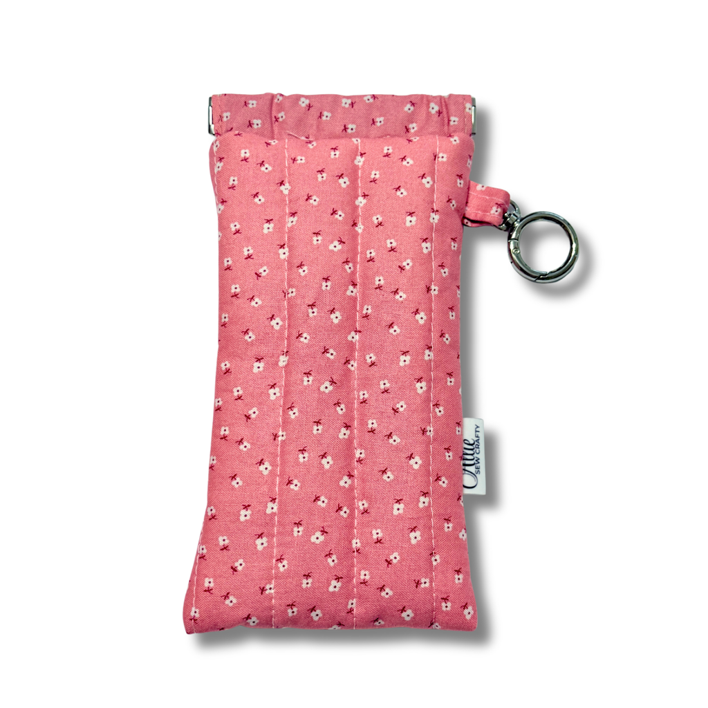A pink fabric pouch with a small white and red floral pattern, featuring a silver metal ring and a white fabric tag with the brand name 'Allie Sew Crafty' printed on it.