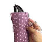 A close-up of a hand holding a purple quilted fabric pouch with a white floral pattern, containing black sunglasses.