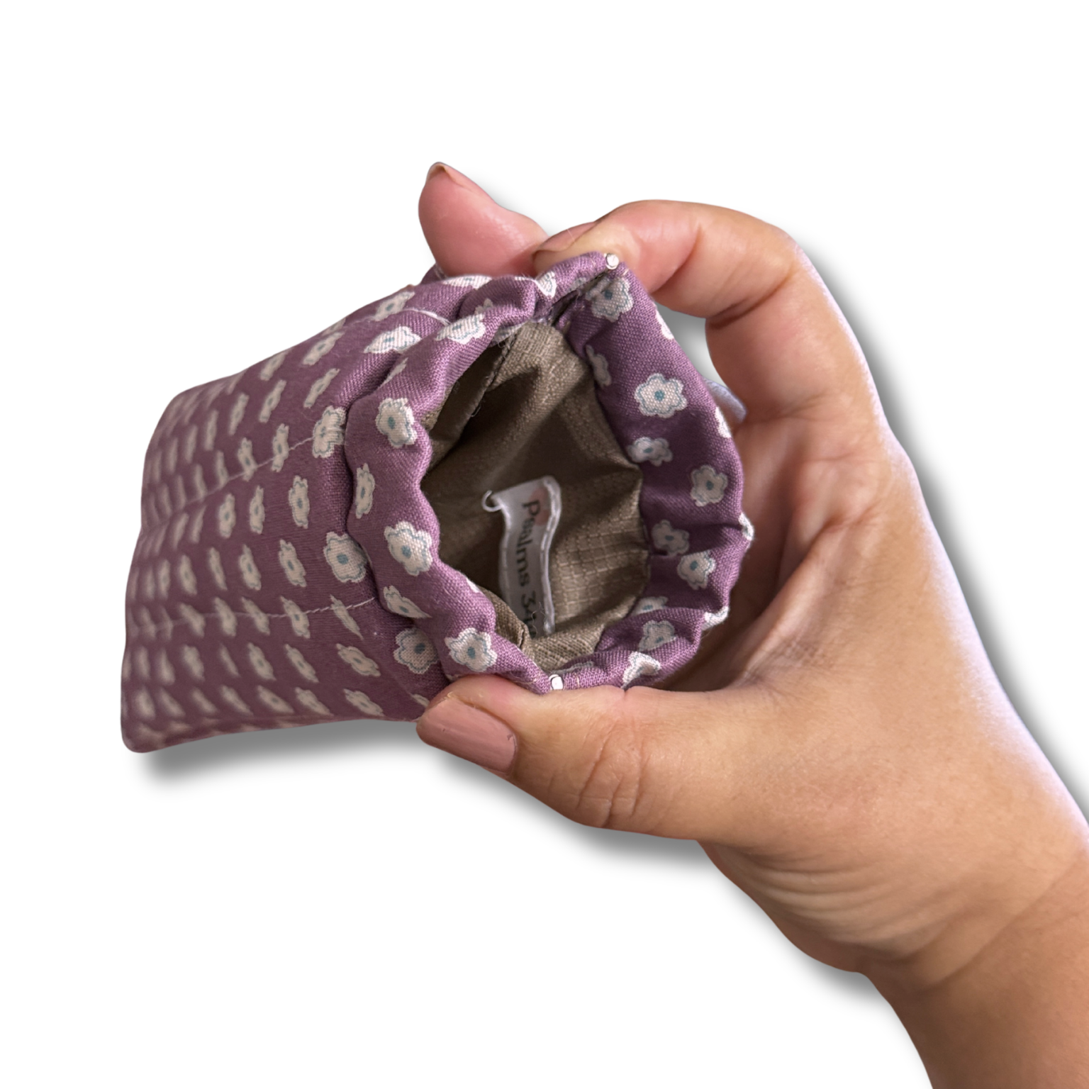 A hand holding a small fabric pouch with a purple and white floral pattern, showing the interior lining and a sewn-in label.