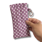 A hand holding a small fabric pouch with a purple and white floral pattern, featuring a metal key ring attachment, set against a plain white background.