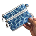A small zippered pouch with a blue and teal geometric pattern, held by a hand against a white background.