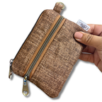 A hand holding a small brown textured zippered pouch with a gold-tone zipper and pull tab, shown against a plain white background.
