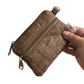 A small brown textured zippered pouch with a gold-tone zipper and pull, held by a hand against a plain white background.