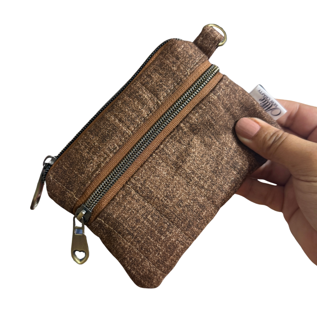 A small brown textured zippered pouch with a gold-tone zipper and pull, held by a hand against a plain white background.
