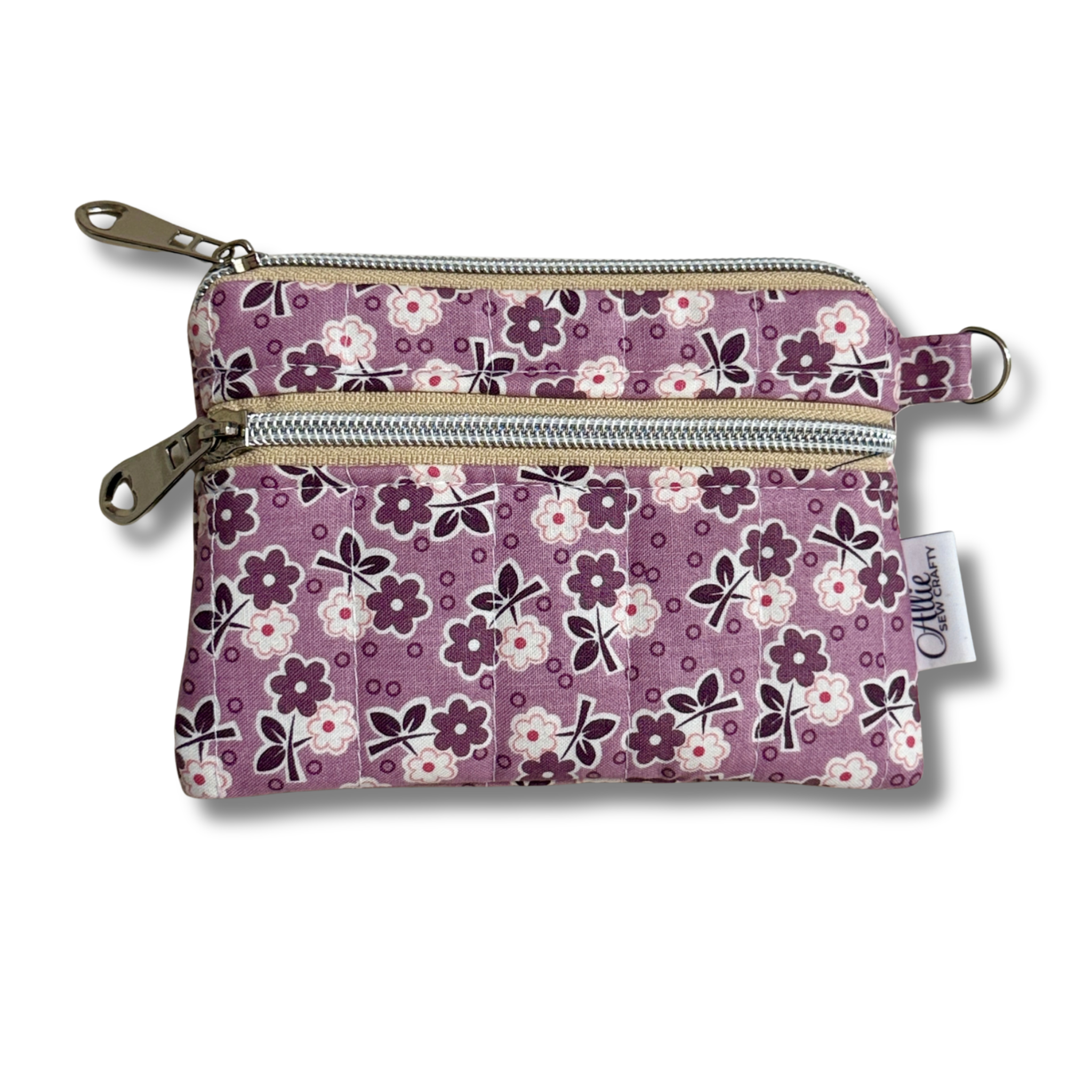 A small fabric zip pouch with a purple floral pattern, featuring two silver zippers, a metal key ring, and a white brand tag that reads 'Allie Sew Crafty'.
