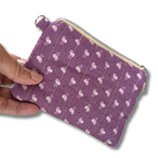 A hand holding a small quilted fabric pouch in lavender purple with a white and pink floral pattern, shown against a plain white background.