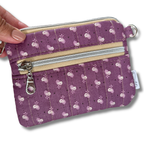 A purple quilted fabric wallet with a white floral pattern, featuring two zippered compartments, a card slot, and a keychain attachment with keys and a car key fob. 