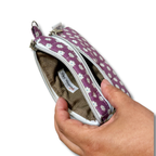 A hand holding open a small zip pouch with a purple and white floral pattern exterior and a brown fabric interior. The brand name 'Paisley Pouch' is visible on the inner label.