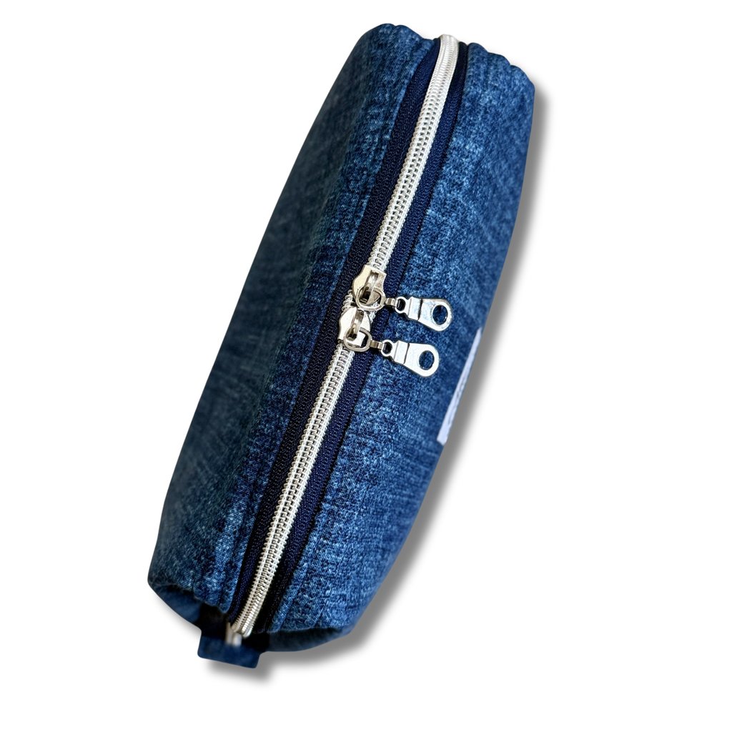 A blue denim pouch with dual silver metal zippers and silver zipper pulls, shown on a plain white background.