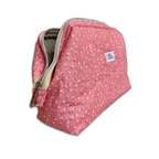 A pink quilted cosmetic pouch with a small white floral pattern, shown with its zipper open on a white background.